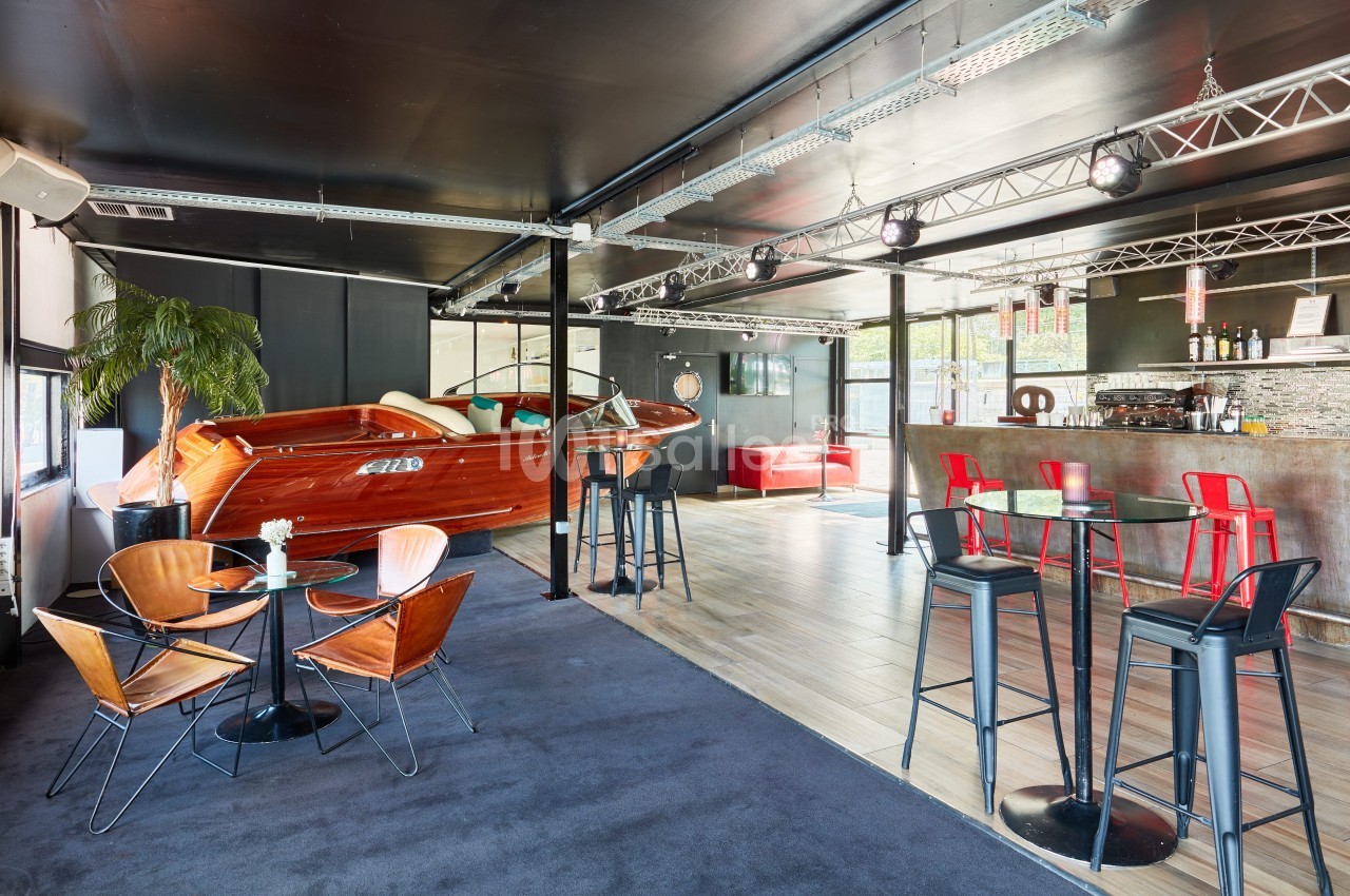 Salle moderne avec bar, tables hautes, fauteuils design et un bateau en bois aménagé en élément décoratif.