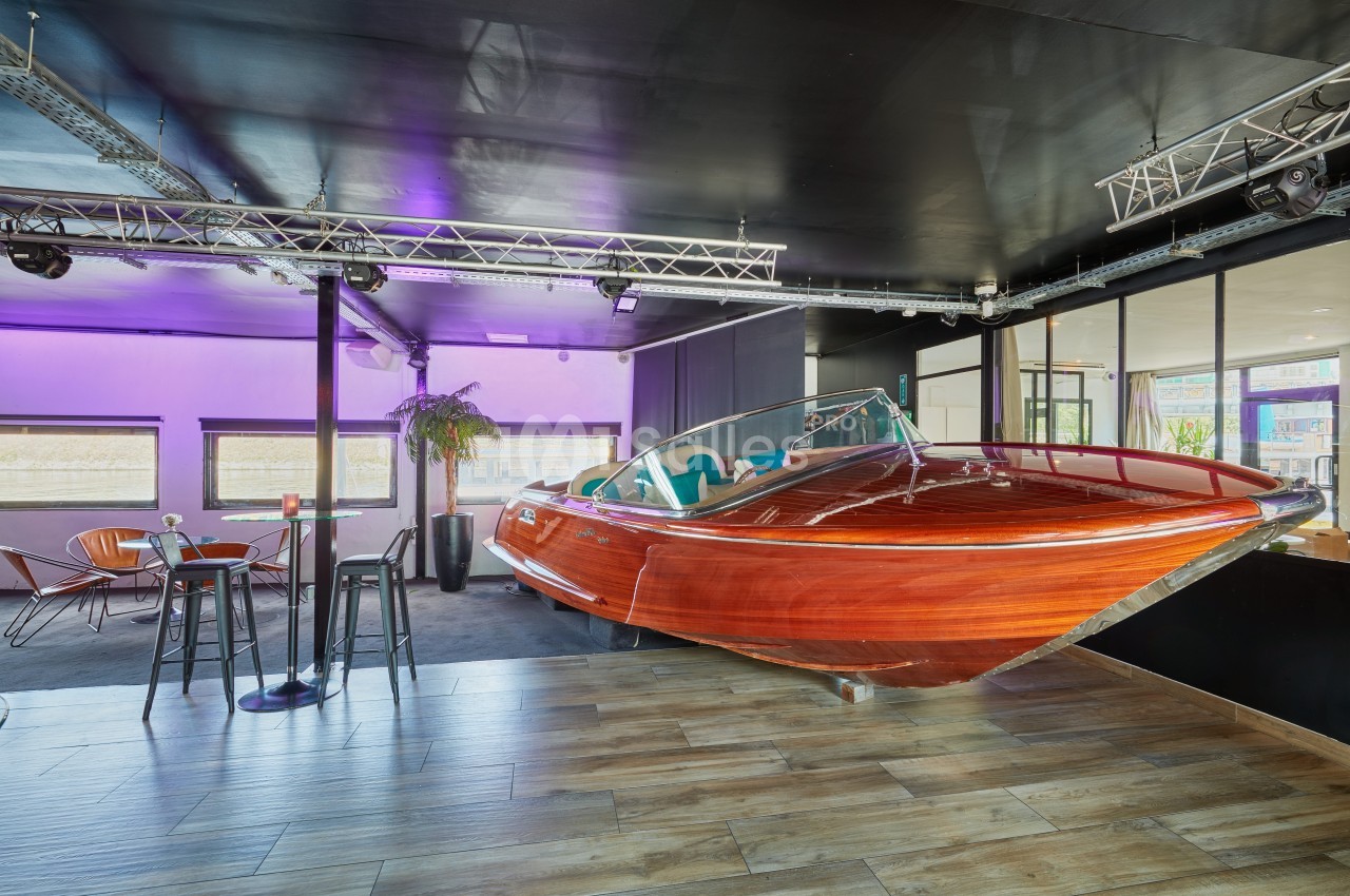 Bateau en bois verni exposé dans un espace intérieur moderne avec éclairage violet et mobilier contemporain.