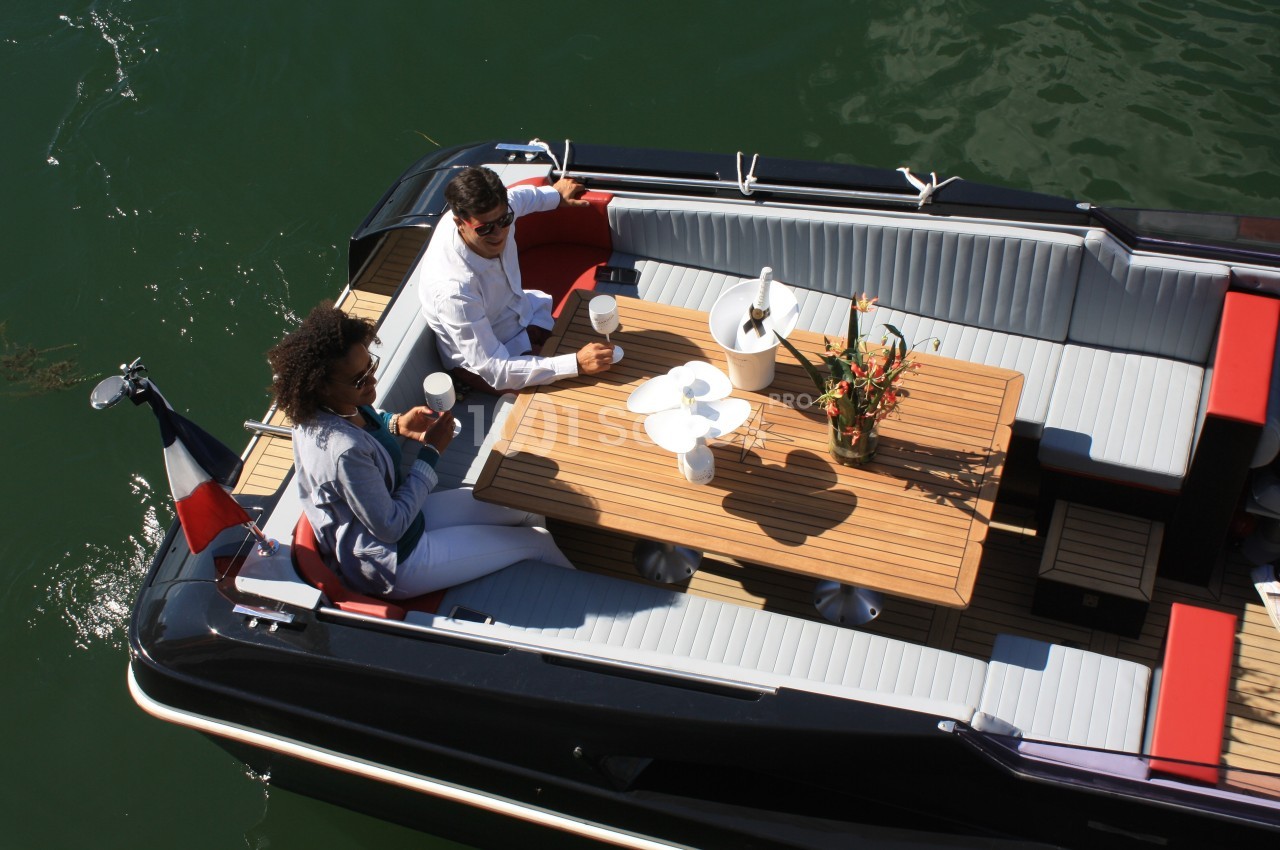 Deux personnes assises à bord d'un bateau, partageant une boisson autour d'une table en bois sur l'eau.