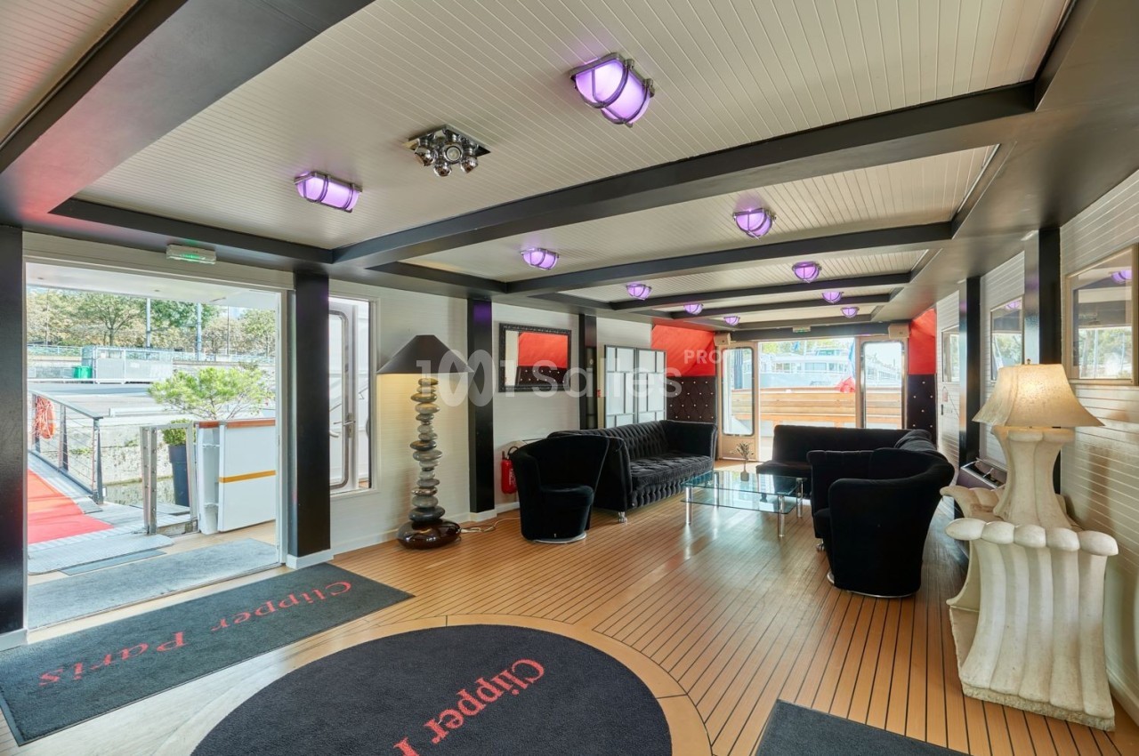 Intérieur lumineux d'un salon avec canapés noirs, lampes design et vue sur l'extérieur par des baies vitrées.