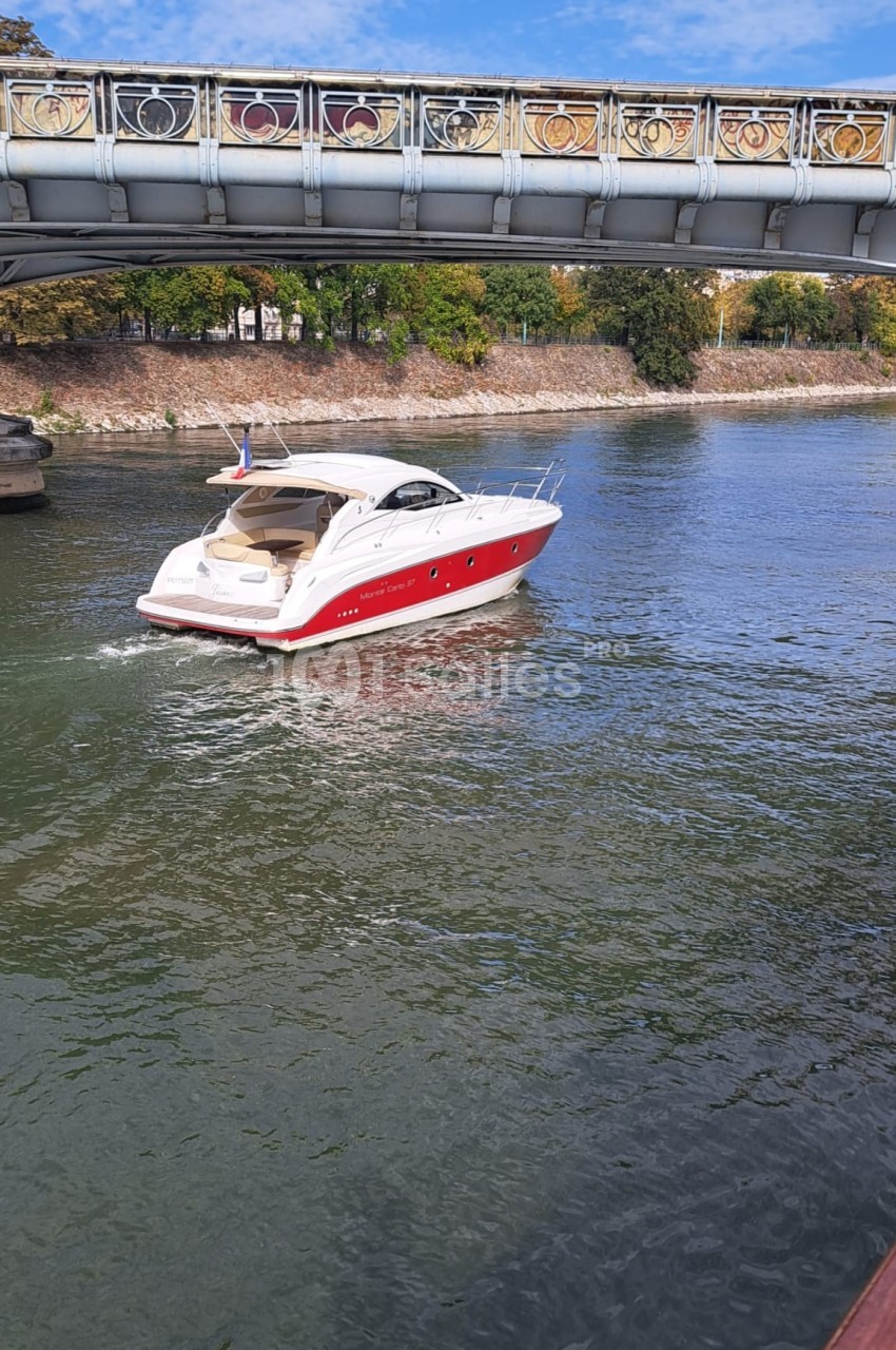 Bateau de plaisance rouge et blanc naviguant sur une rivière sous un pont décoré.