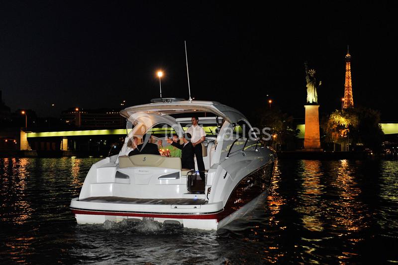 Un bateau de plaisance navigue de nuit sur une rivière, avec la tour Eiffel et une statue en arrière-plan.