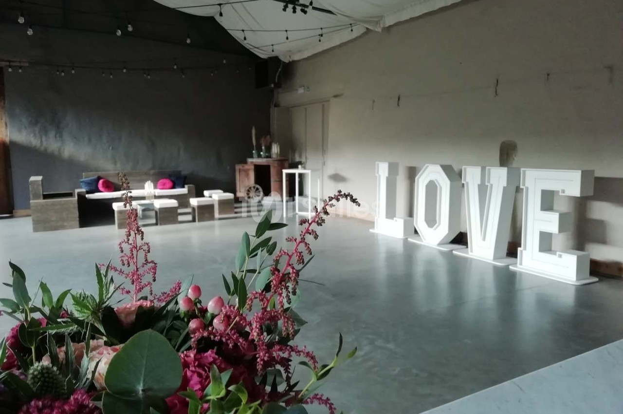 Salle décorée pour un événement avec des fleurs au premier plan et des lettres lumineuses formant ’LOVE’ en arrière-plan.