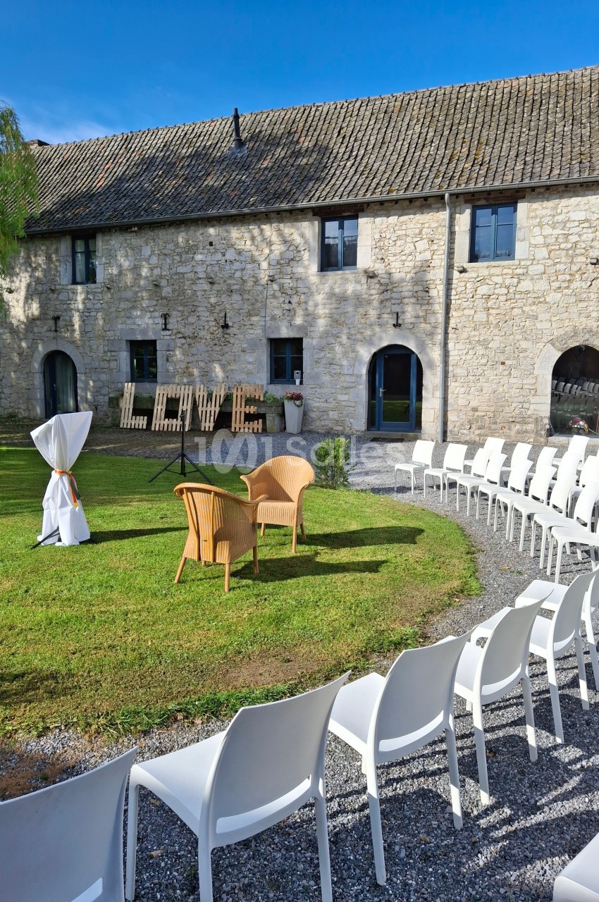Chaises blanches disposées en cercle sur une pelouse devant une grange en pierre, avec le mot ’LOVE’ en décor.