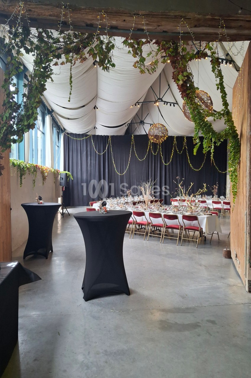 Salle de réception décorée avec des guirlandes lumineuses, des tables dressées et des chaises rouges.