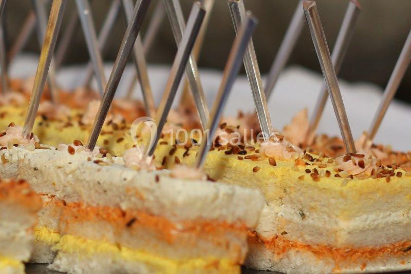 Assortiment de mini-sandwichs garnis de différentes couches colorées, décorés de graines et piqués de bâtonnets.