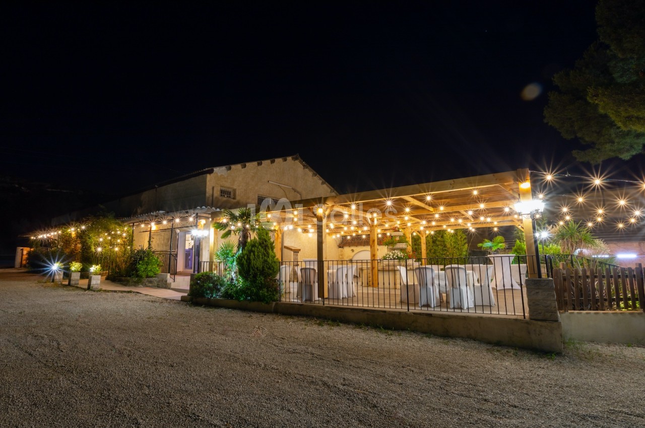 Terrasse éclairée d'un bâtiment en soirée, décorée de guirlandes lumineuses et aménagée avec des tables dressées.