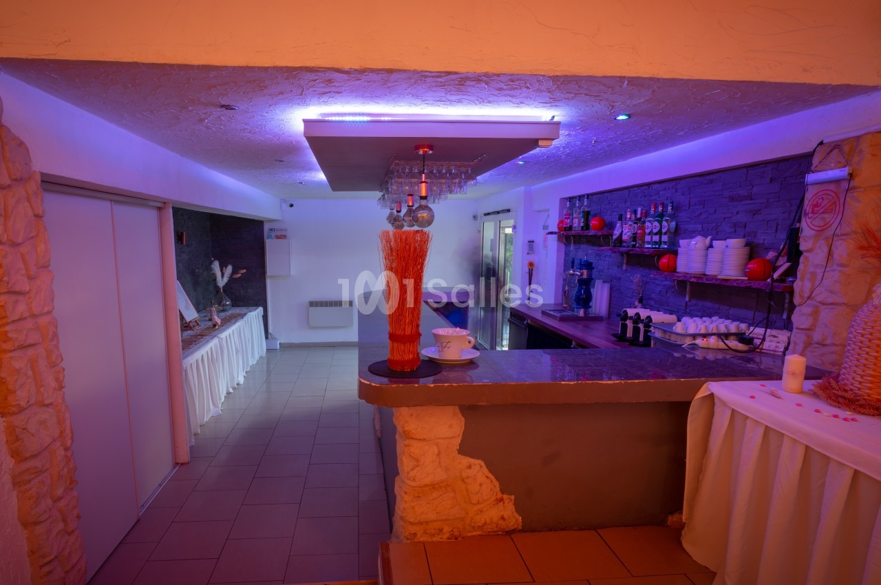 Bar avec comptoir en pierre, étagères de bouteilles, lumière violette et décoration minimaliste.