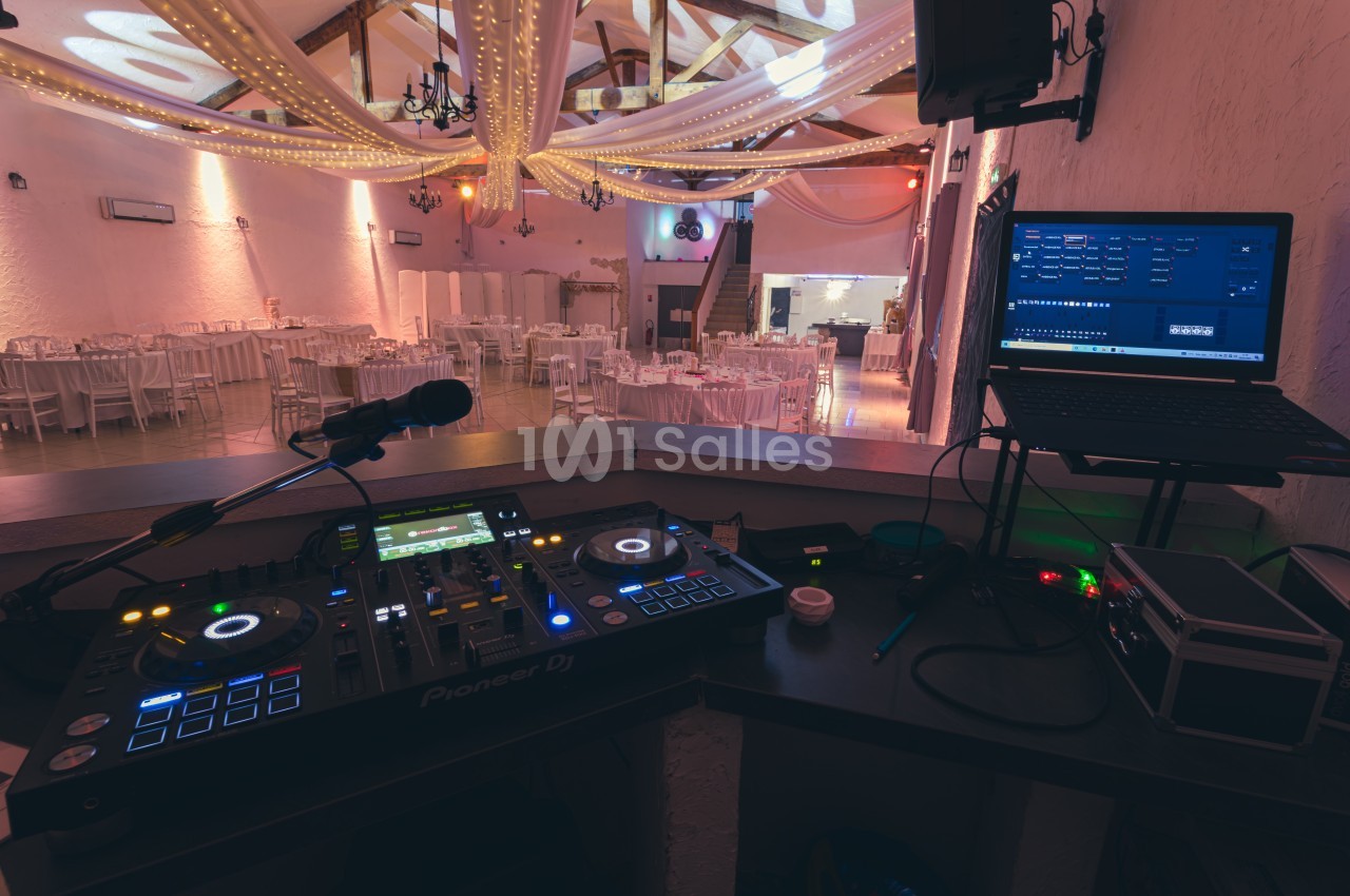 Console de DJ avec platines et ordinateur dans une salle de réception décorée de guirlandes lumineuses.