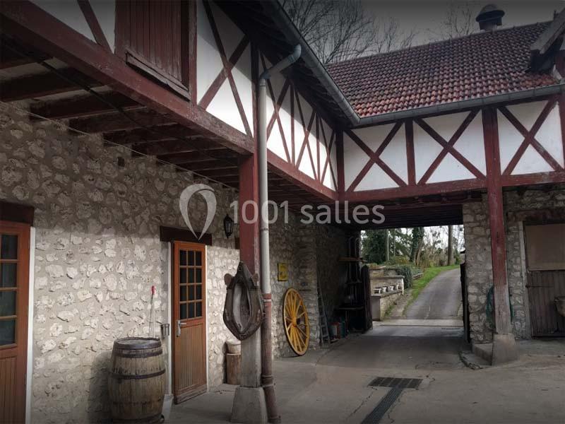 Bâtiment en pierre avec colombages, porte en bois, barrique et roue ancienne, donnant sur une allée pavée.