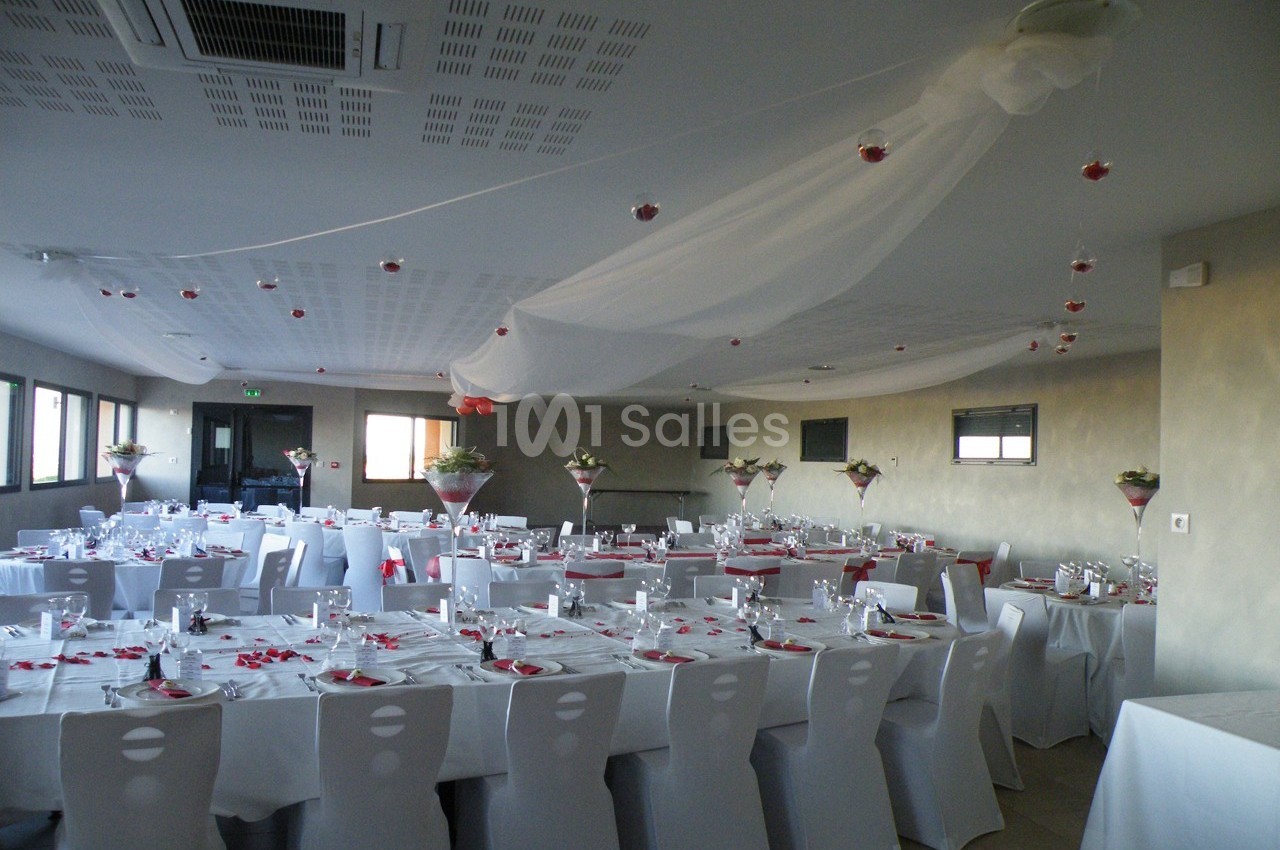 Salle de réception décorée avec des tables dressées, nappes blanches et centres de table fleuris.