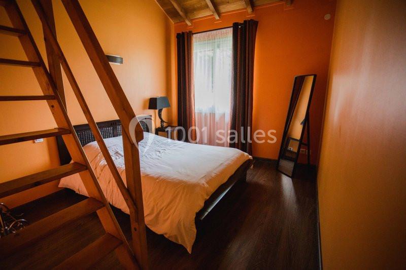 Chambre avec murs orange, lit double, miroir sur pied, lampe de chevet et échelle menant à une mezzanine en bois.