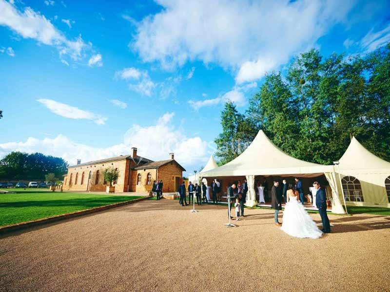 Un mariage en plein air avec des invités rassemblés près de tentes blanches dans un cadre verdoyant et ensoleillé.