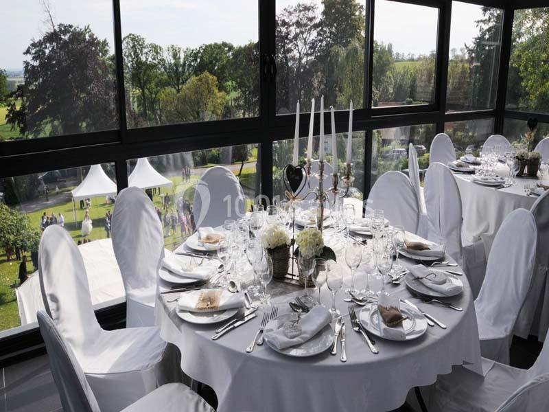 Table élégamment dressée avec nappes blanches, chandeliers et vaisselle raffinée, dans une salle vitrée avec vue sur un…