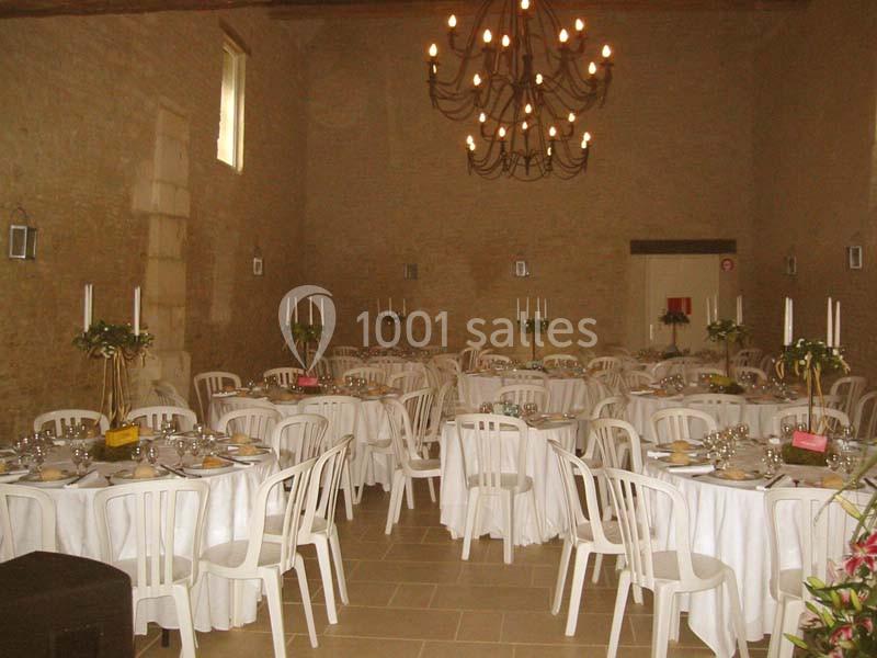Salle de réception décorée avec des tables rondes dressées, nappes blanches et chandeliers suspendus.