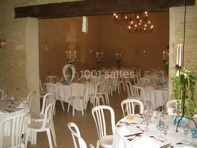 Salle de réception décorée avec des tables rondes, nappes blanches, chaises en plastique et chandeliers suspendus.
