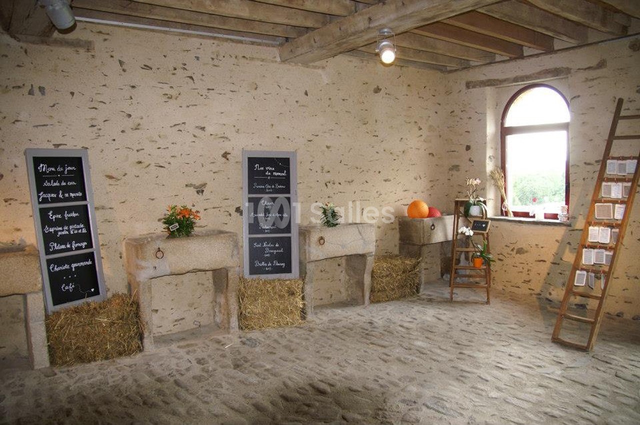 Intérieur d'une salle rustique avec murs en pierre, ardoises inscrites, bottes de paille et décorations végétales.