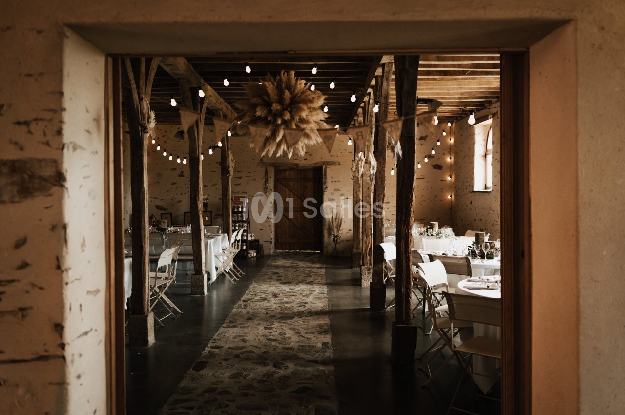 Salle rustique avec tables dressées, guirlandes lumineuses suspendues et décoration en bottes de paille au plafond.