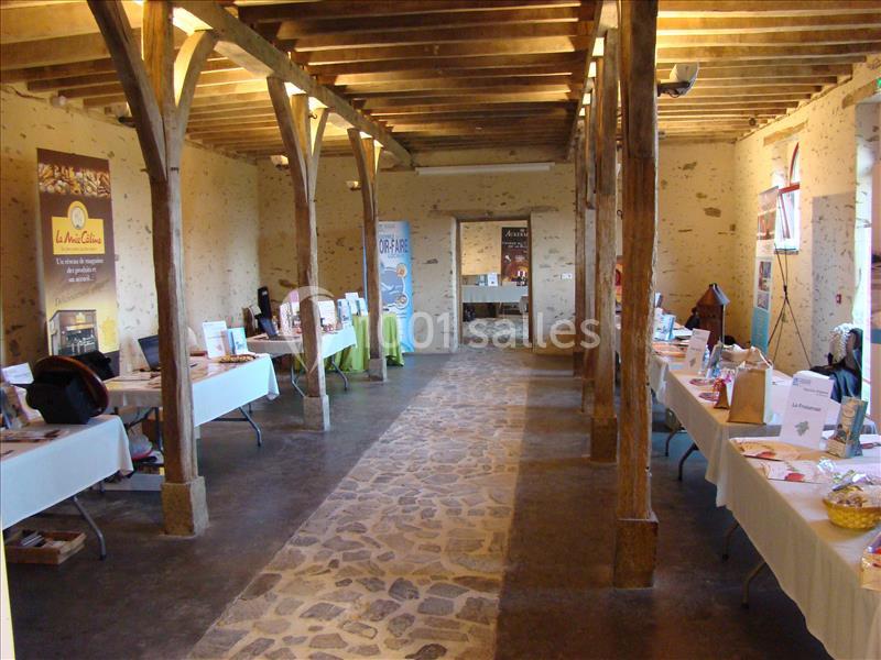Salle en pierre avec poutres apparentes, tables alignées présentant des documents et objets lors d'un événement.
