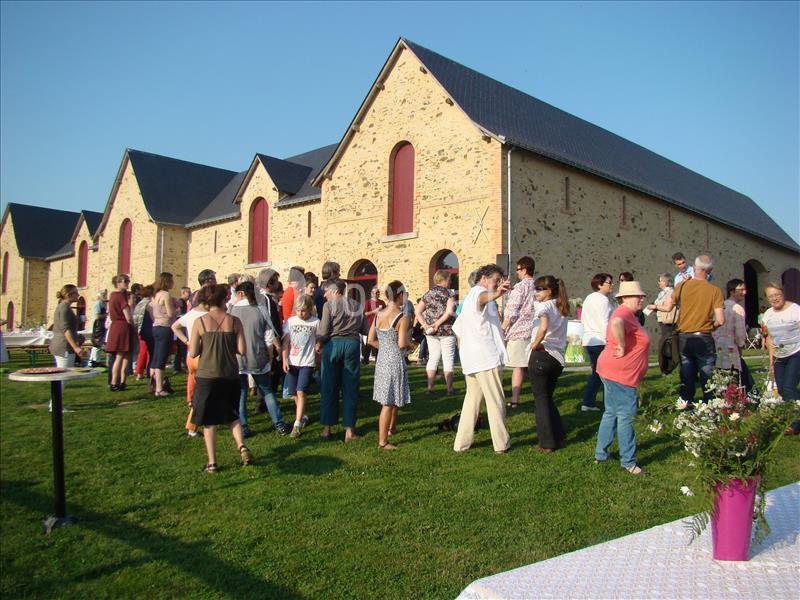 Groupe de personnes discutant en plein air devant de grands bâtiments en pierre avec des toits en ardoise.