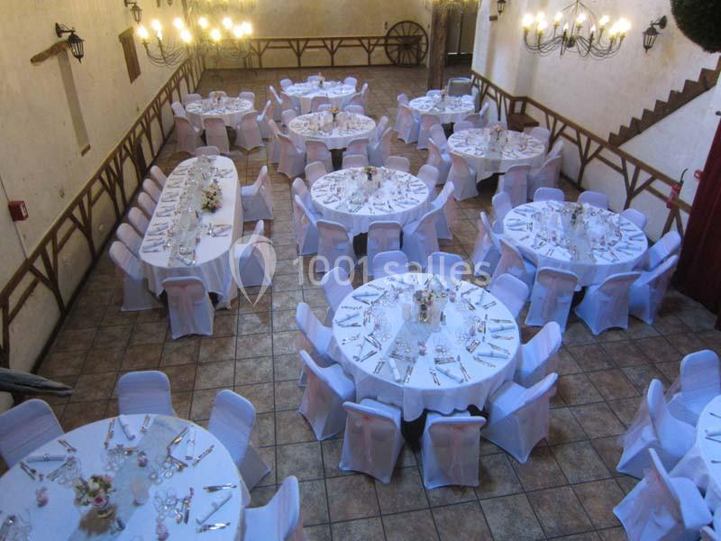 Salle de réception décorée avec des tables rondes et ovales dressées, chaises blanches et éclairage suspendu.