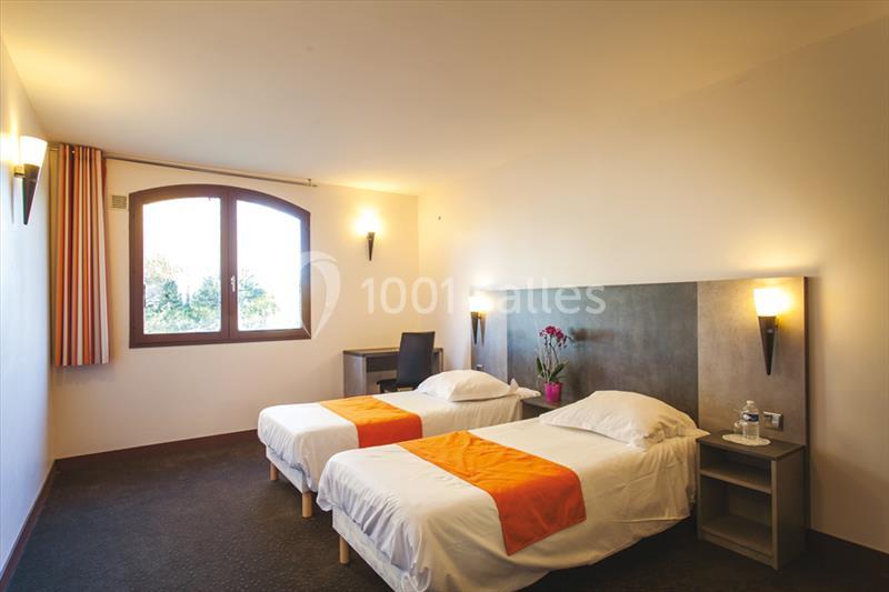 Chambre avec deux lits simples, linge blanc et chemins de lit orange, bureau près d'une fenêtre avec vue extérieure.