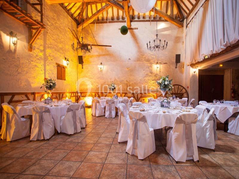 Salle de réception décorée avec des tables rondes, nappes blanches et arrangements floraux, éclairage chaleureux.