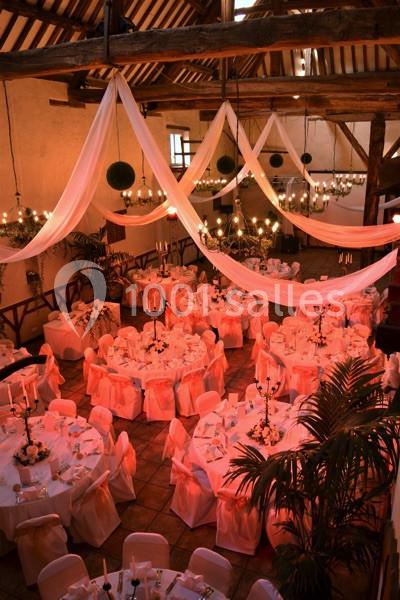 Salle de réception décorée avec des tables rondes, nappes blanches, chaises ornées de rubans et drapés suspendus.