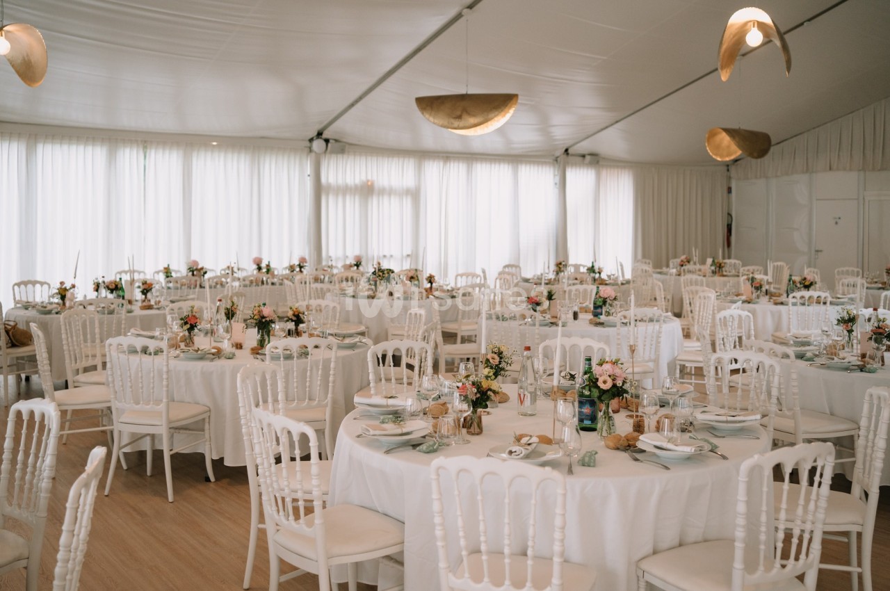 Salle de réception décorée avec des tables rondes, nappes blanches, chaises assorties et arrangements floraux.