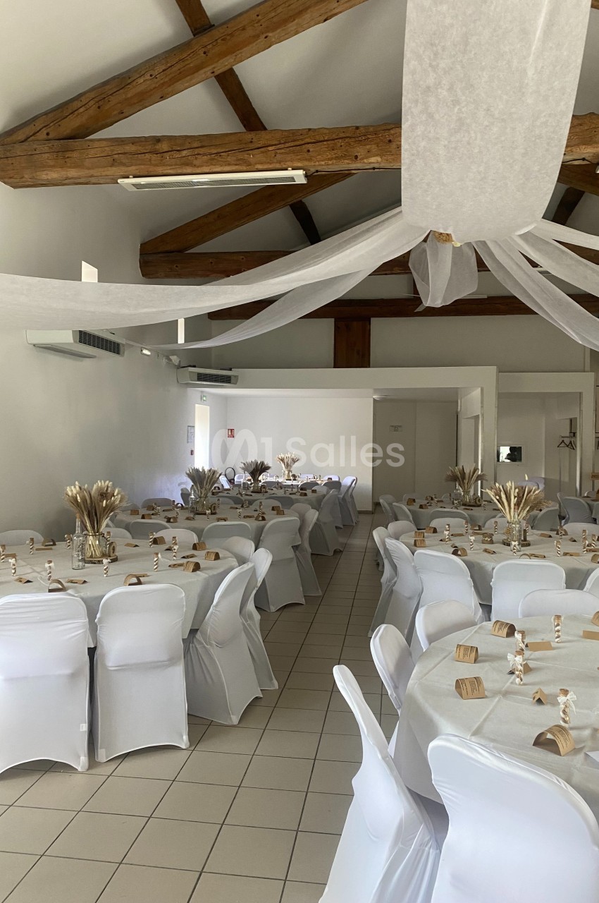 Salle de réception décorée avec des tables rondes, nappes blanches, chaises houssées et ornements en tons naturels.