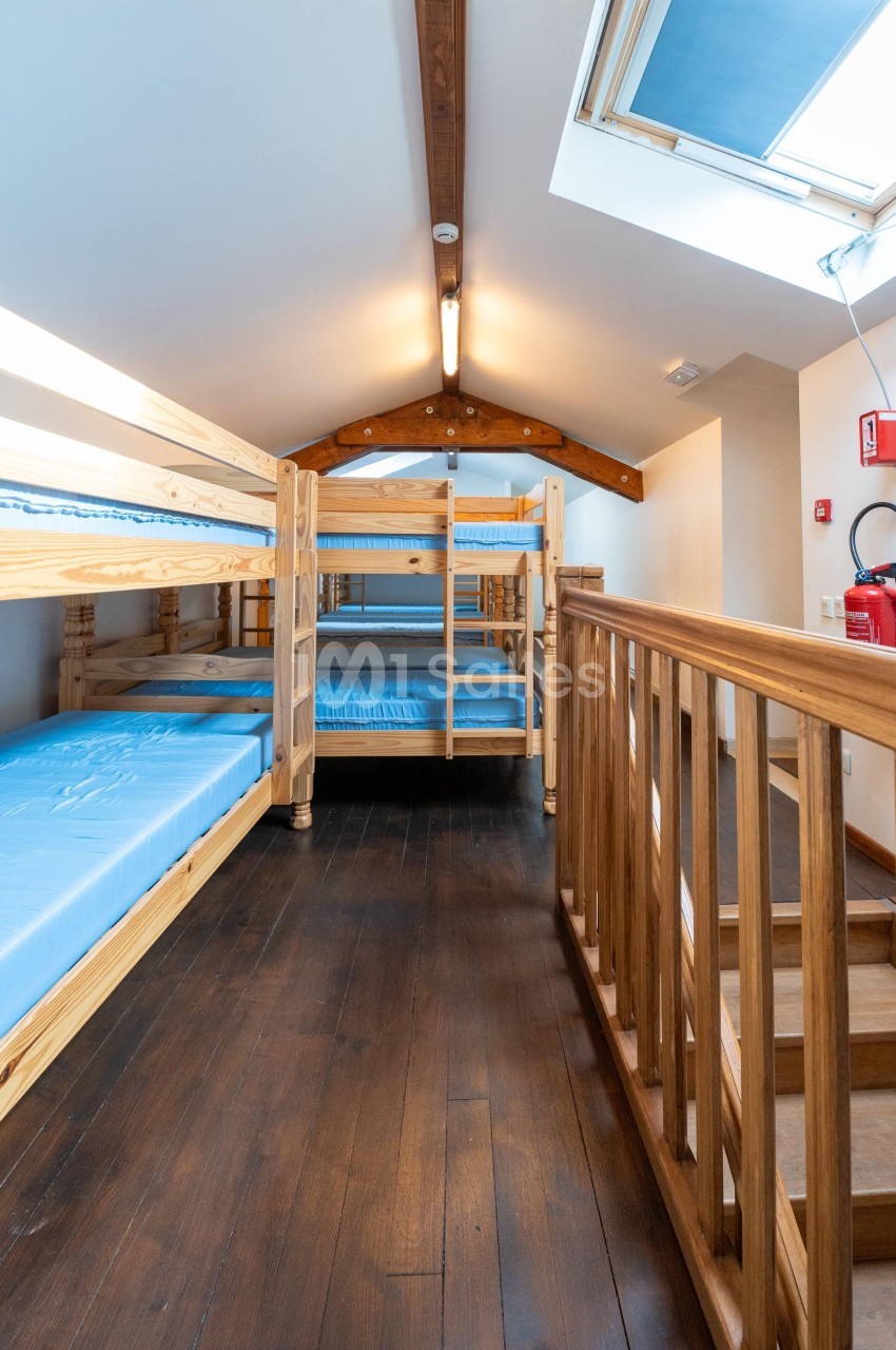 Dortoir avec lits superposés en bois, matelas bleus, parquet sombre et lumière naturelle provenant d'une fenêtre de toit.