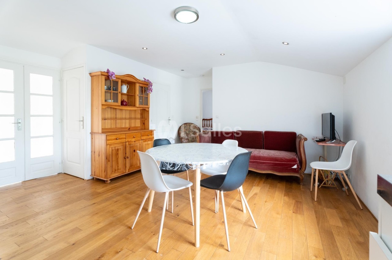Salle à manger lumineuse avec table ronde, chaises modernes, buffet en bois, canapé rouge et parquet clair.