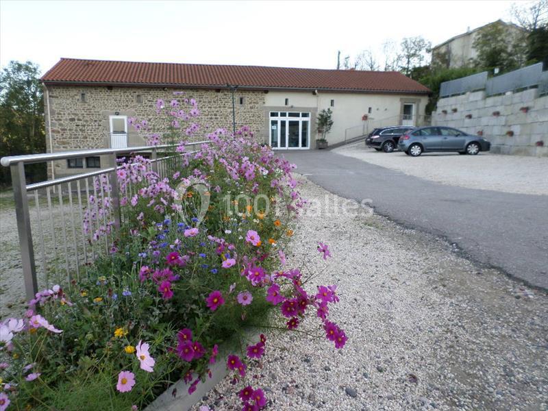 Massif de fleurs colorées bordant une allée menant à un bâtiment en pierre avec toit en tuiles rouges.