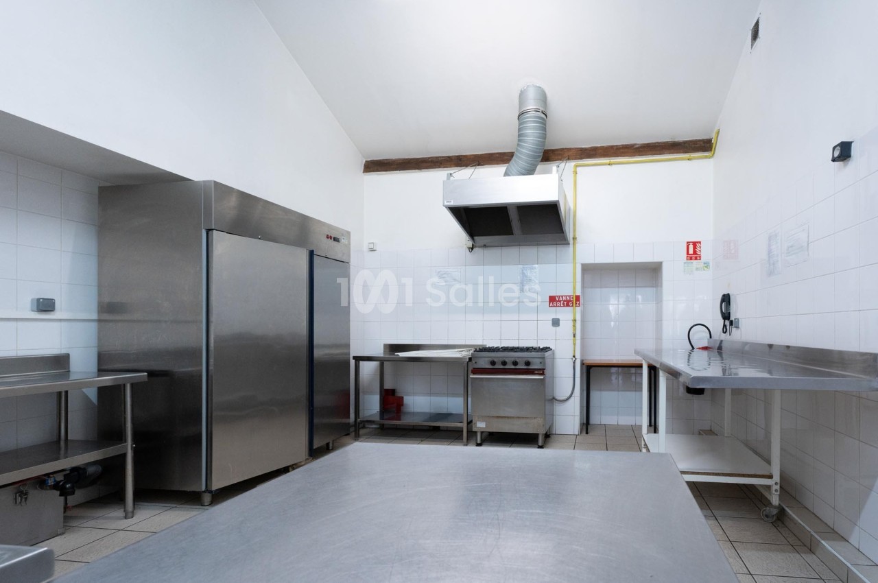 Cuisine professionnelle avec équipements en inox, comprenant un réfrigérateur, une hotte, un four et des plans de travail.