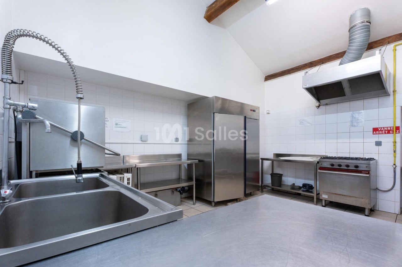 Cuisine professionnelle avec évier inox, réfrigérateur, hotte, plaques de cuisson et plan de travail en acier.