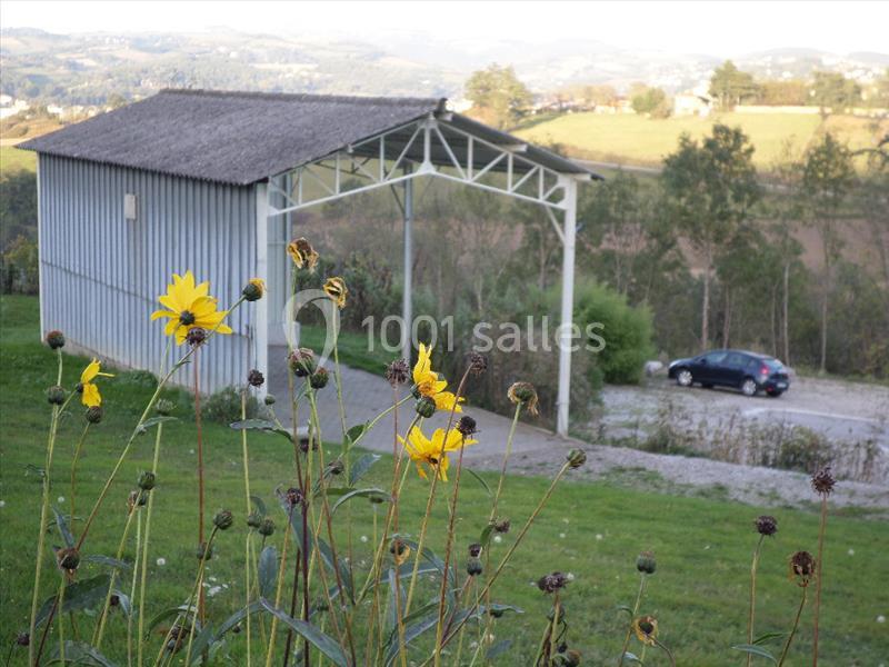 Des tournesols fanés au premier plan devant un abri métallique dans un paysage rural vallonné.