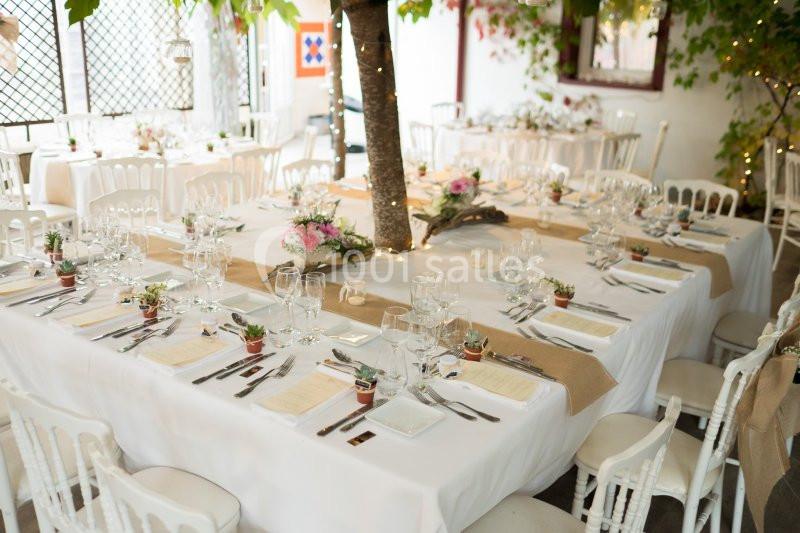 Tables décorées pour un événement, avec nappes blanches, chemins de table en toile de jute et arrangements floraux.