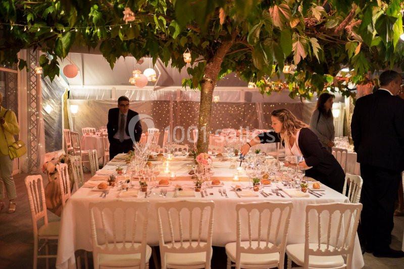 Table décorée pour un dîner sous un arbre, avec des bougies allumées et des invités en arrière-plan.