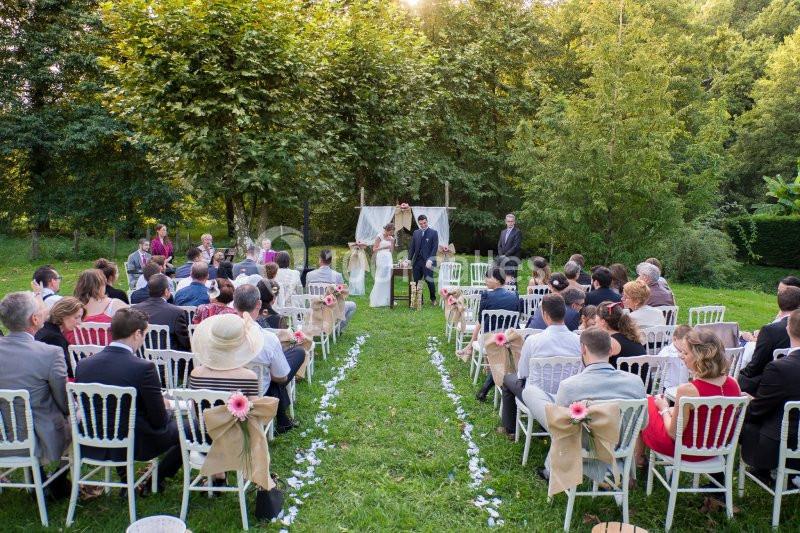 Cérémonie de mariage en plein air avec des invités assis, un couple devant un autel décoré, entouré de verdure.