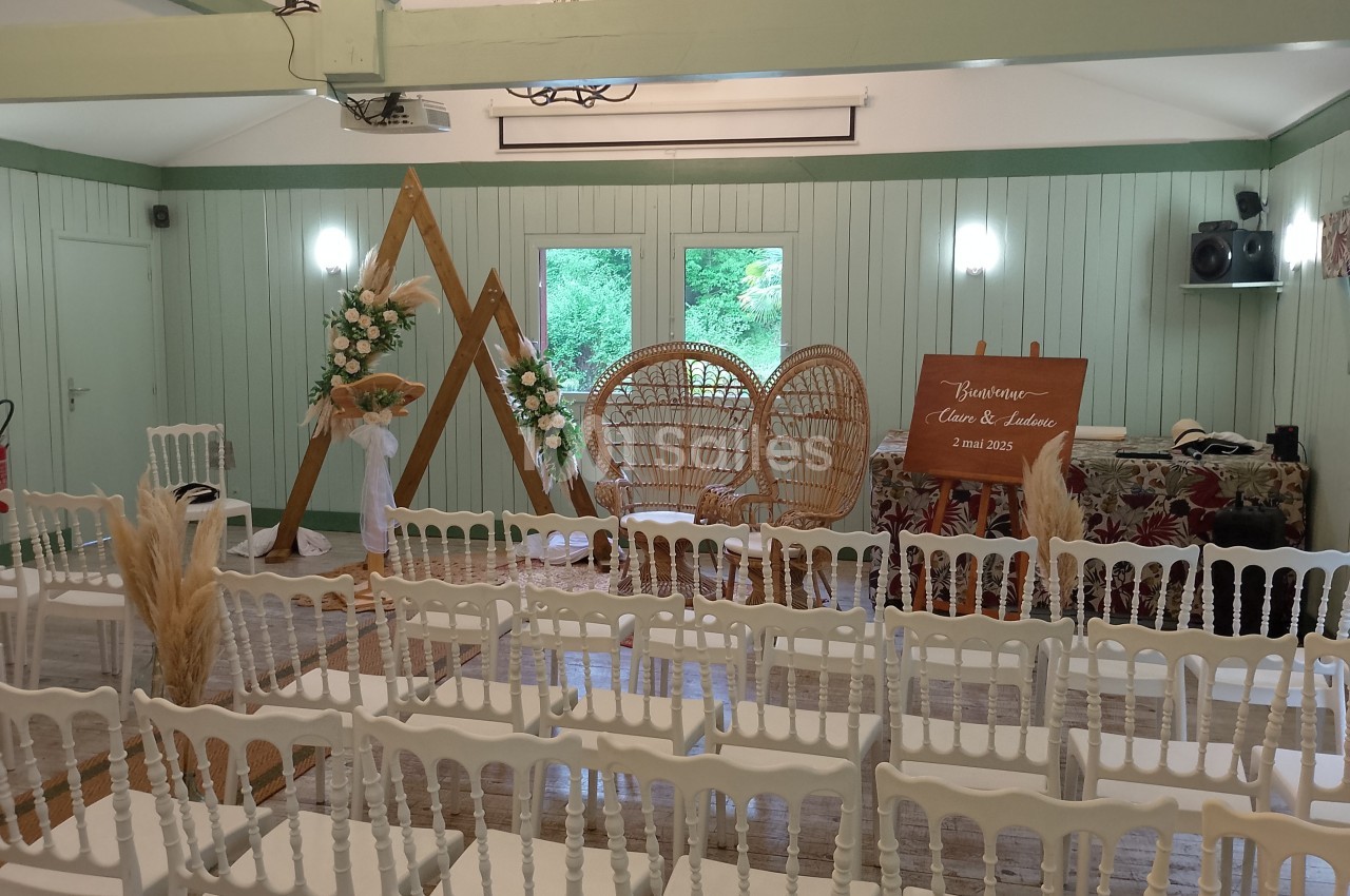 Salle décorée pour un mariage avec des chaises blanches, un panneau de bienvenue et des éléments floraux naturels.