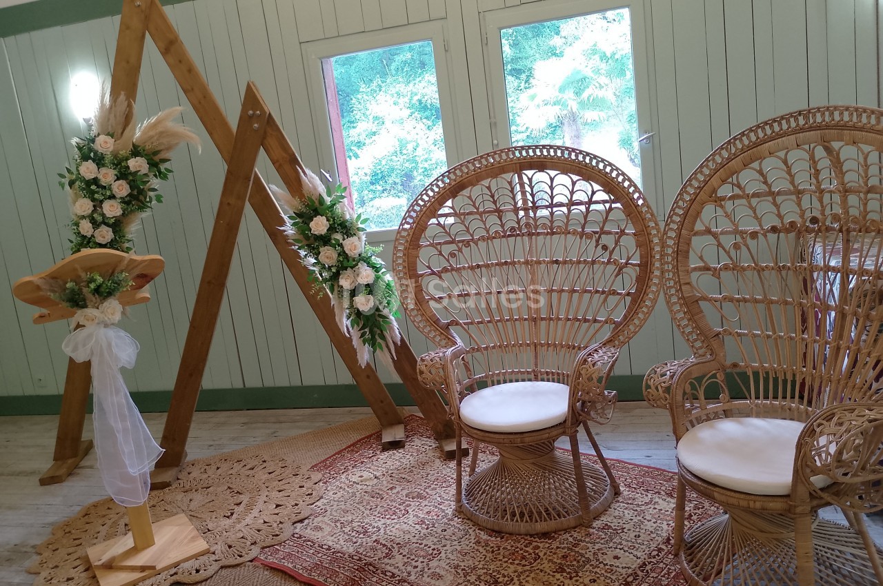 Décoration intérieure avec deux fauteuils en rotin, un pupitre fleuri et une arche triangulaire ornée de fleurs.