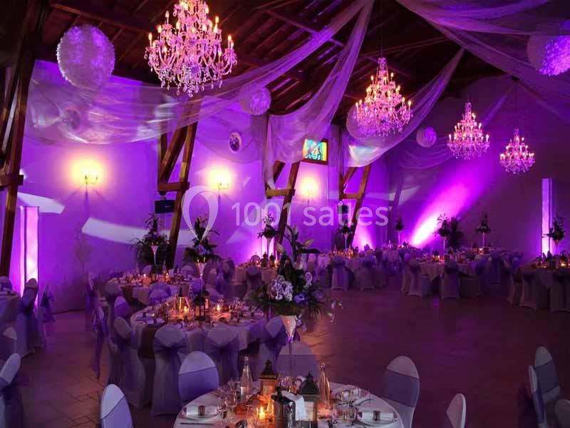 Salle de réception décorée avec des tables dressées, éclairage violet et lustres suspendus au plafond.