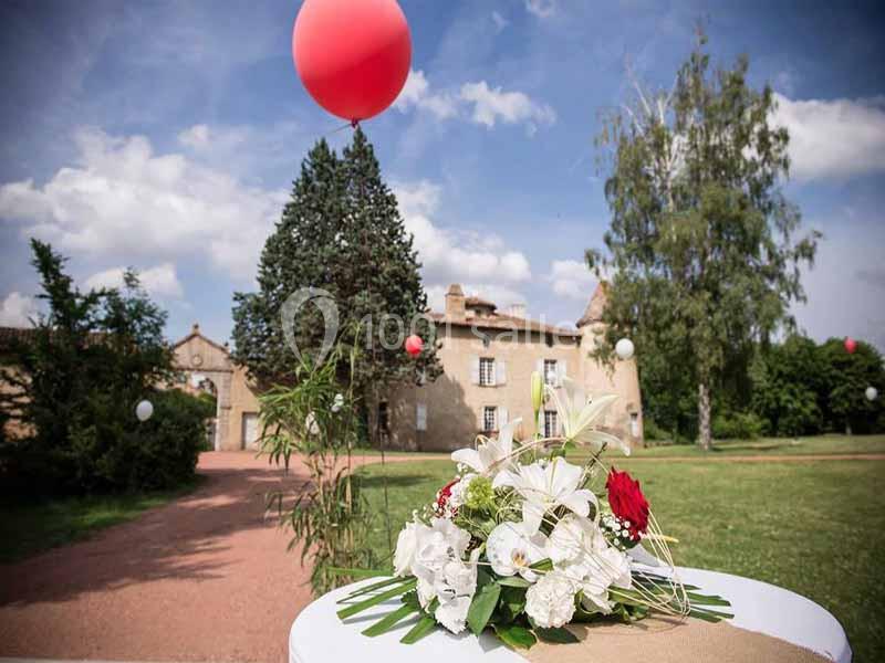 Bouquet de fleurs blanches et rouges posé sur une table en extérieur, avec un manoir et des ballons en arrière-plan.