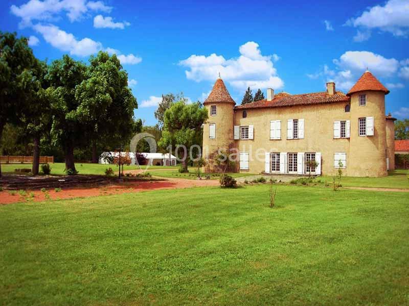 Manoir ancien avec tours rondes, entouré de pelouses et d'arbres sous un ciel bleu dégagé.