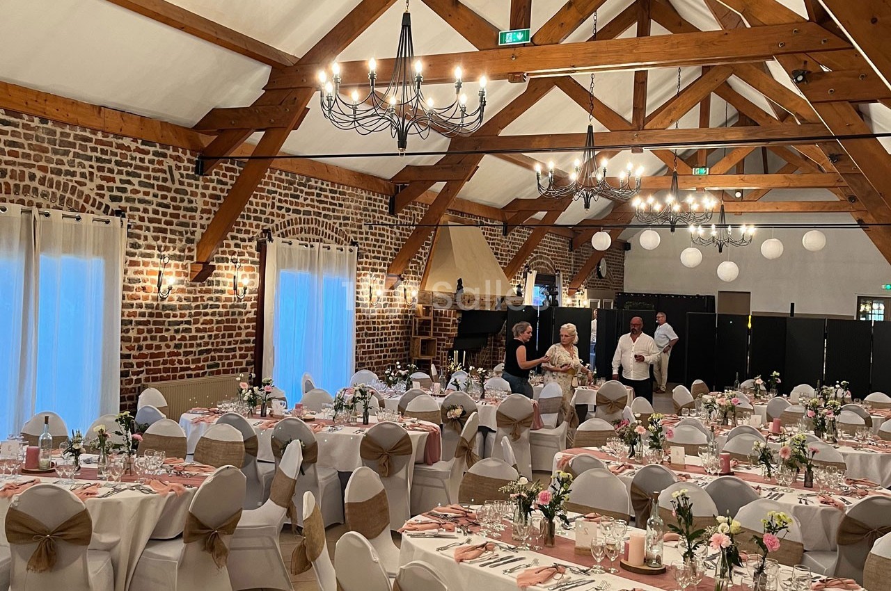 Salle de réception décorée avec des tables dressées, des chaises ornées et des poutres apparentes en bois.