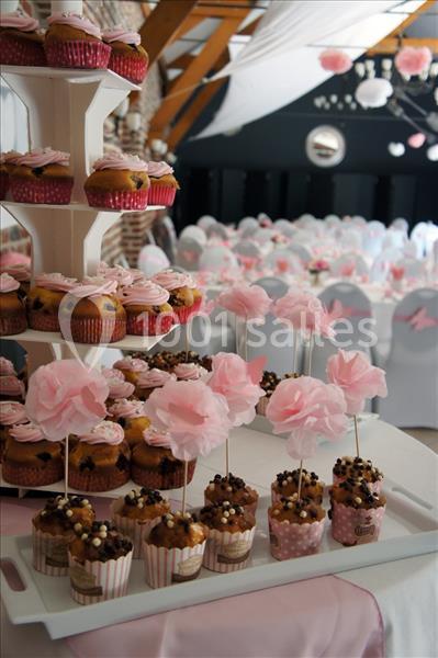 Présentoir de cupcakes décorés et table ornée de fleurs en papier rose dans une salle de réception.