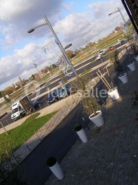 Vue d'un parking vide avec quelques véhicules, des lampadaires et des jardinières blanches sur un trottoir pavé.