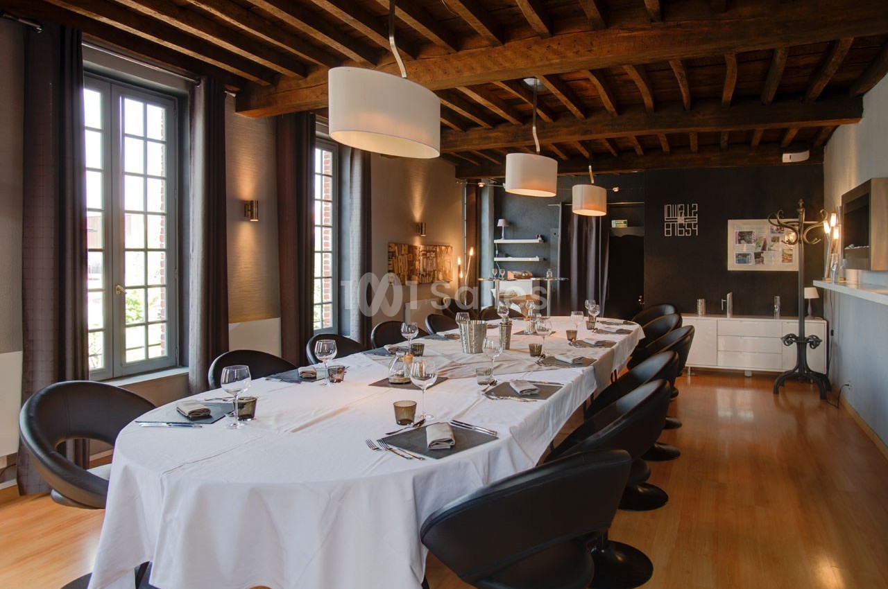 Salle à manger élégante avec une grande table dressée, des chaises noires et un plafond en bois apparent.