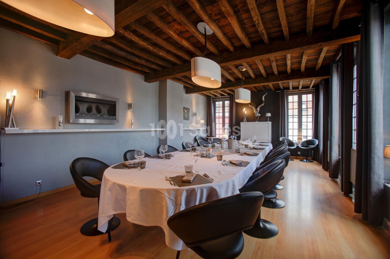 Salle à manger élégante avec grande table dressée, chaises noires, plafond en bois et lumière naturelle.