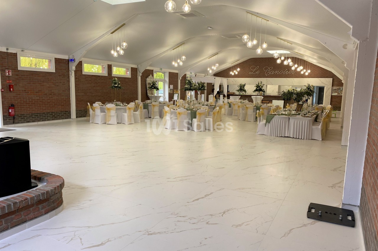 Salle de réception lumineuse avec tables décorées, chaises blanches et murs en briques rouges.